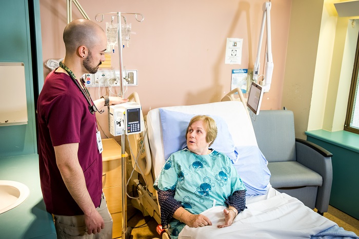 Infirmier dans une chambre d’hôpital avec une patiente assise dans un lit d’hôpital.
