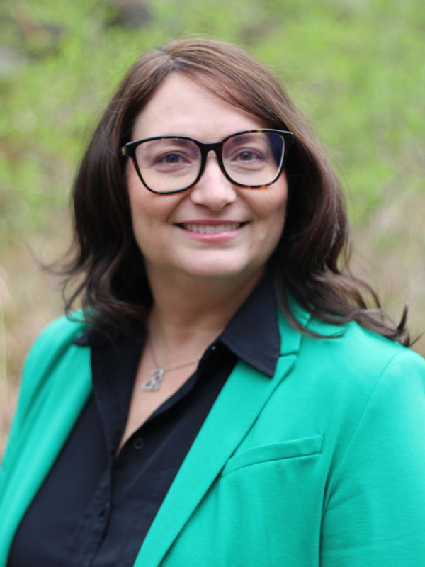 Lesley Mallen - a middle aged woman with short dark hair and glasses wearing a bright green jacket