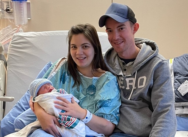 Jeune couple assis sur un lit d’hôpital tenant un nouveau-né dans les bras.