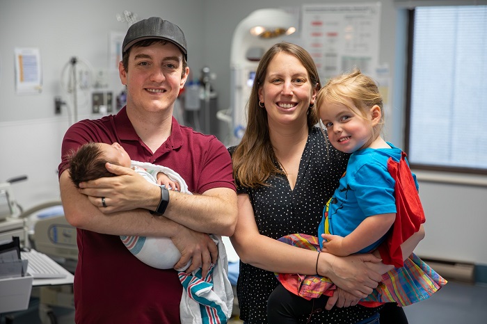 Parents qui tiennent un bébé et un jeune enfant dans les bras, dans une chambre d’hôpital.
