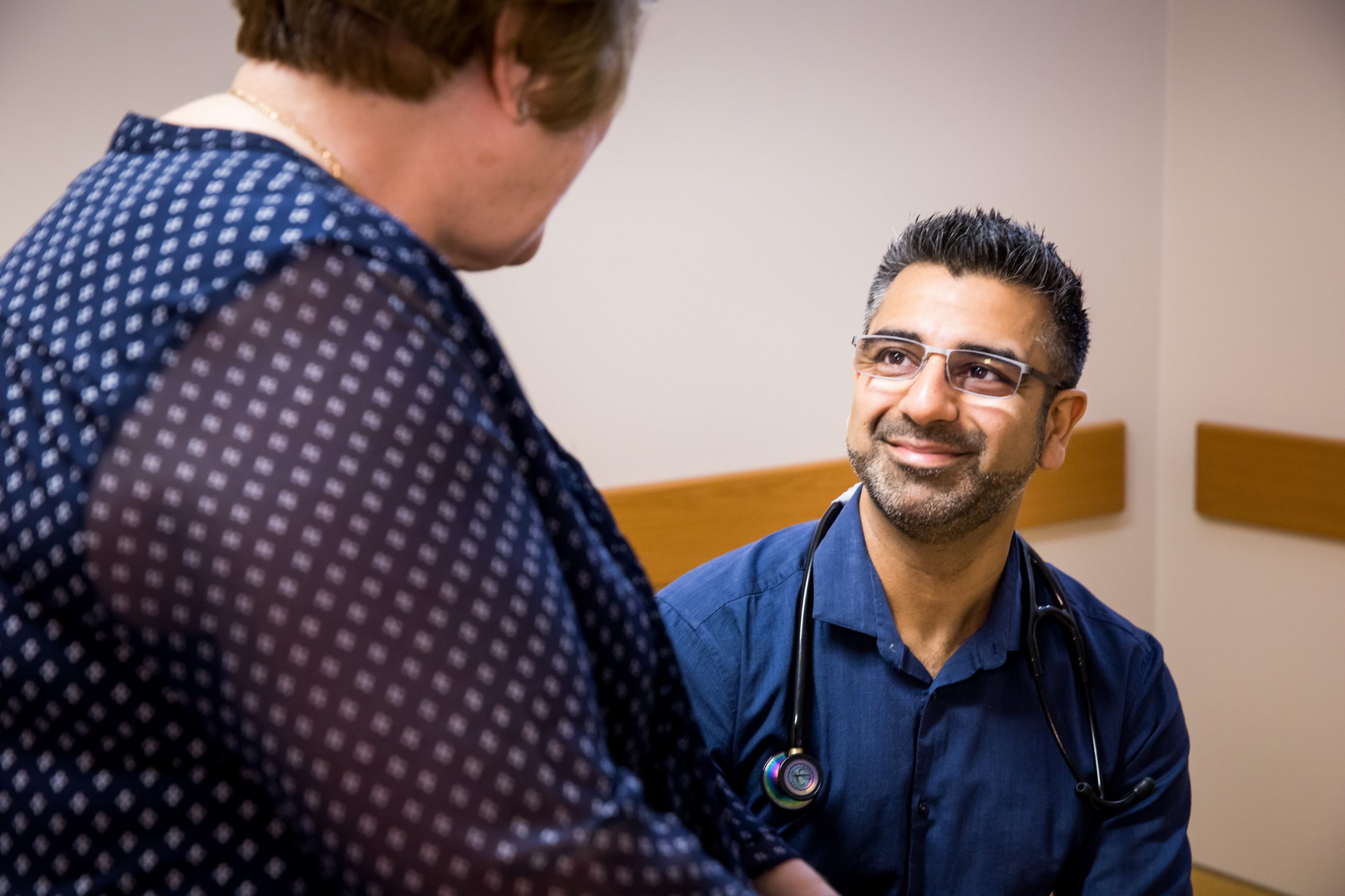 A man with short hair and glasses wearing a stethoscope looks up at a woman smiling.