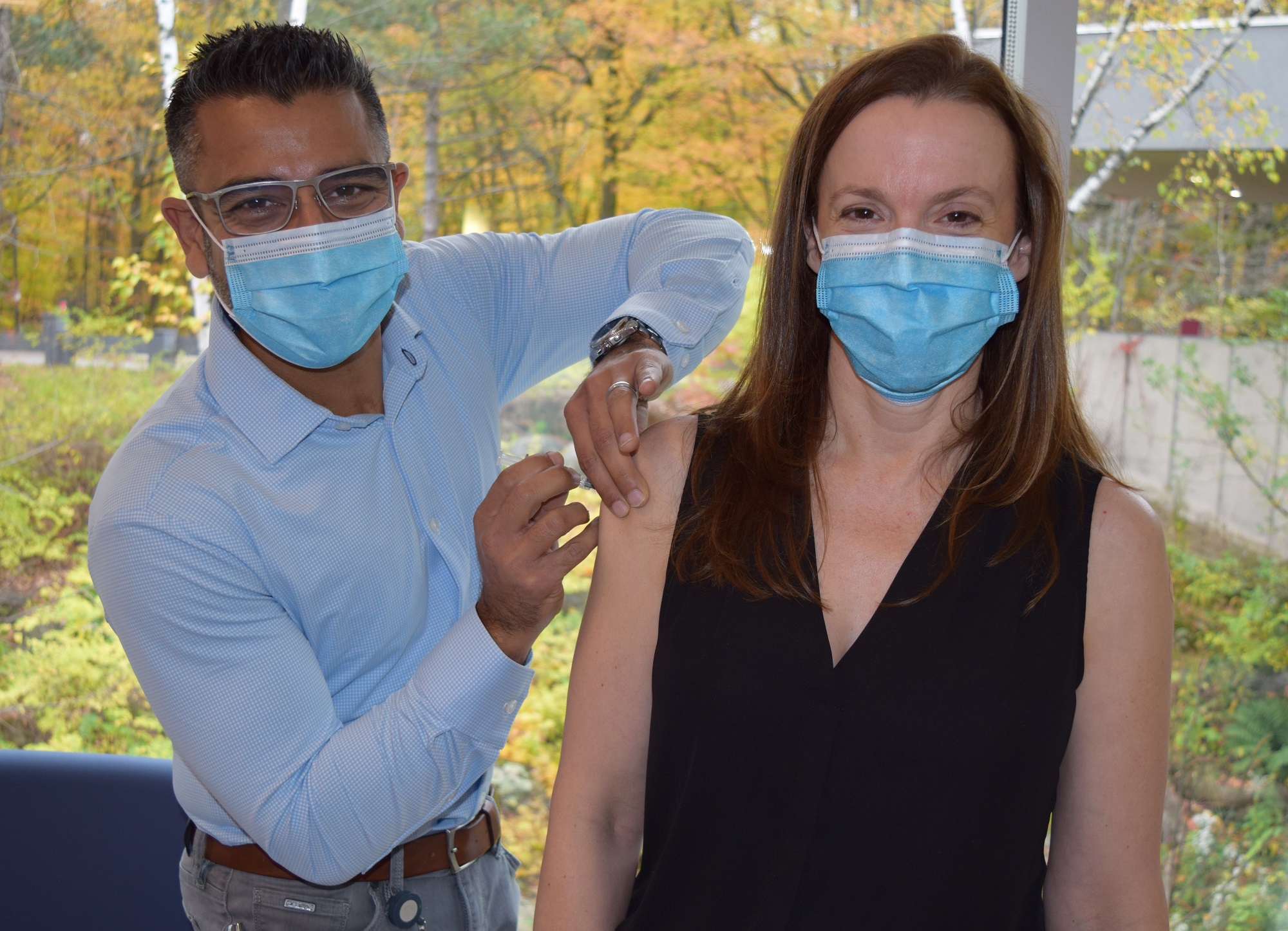 Doctor wearing a mask gives a flu shot to a woman who is also in a mask.