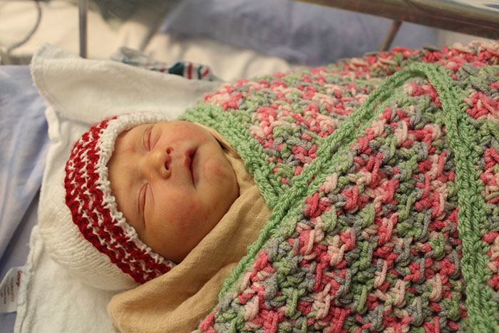 A sleeping baby wearing a knitted hat and wrapped in a crochet pink and green blanket.