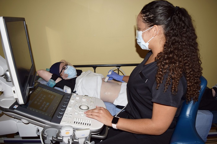 A female staff member is working an ultra sound machine while a patient lies beside her.