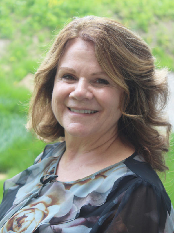 Linda Gravel - a woman with short wavy brown hair wearing a brown and black floral top