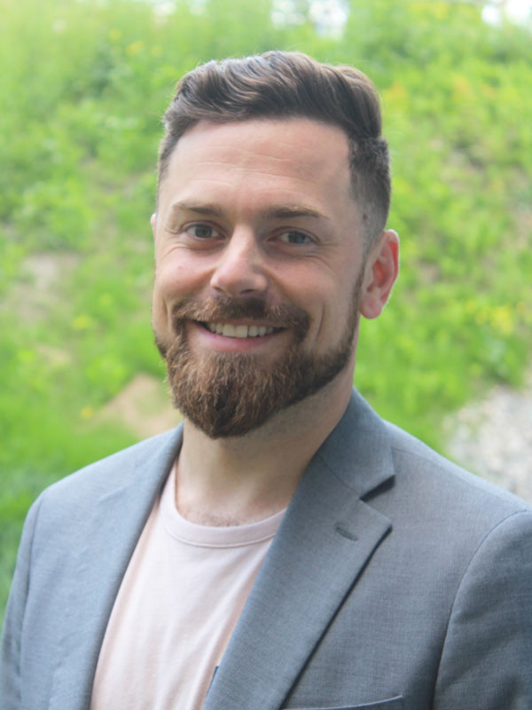 Sean Molnar - man with short styles brown hair and reddish beard wearing a light grey blazer over a pale pink t-shirt