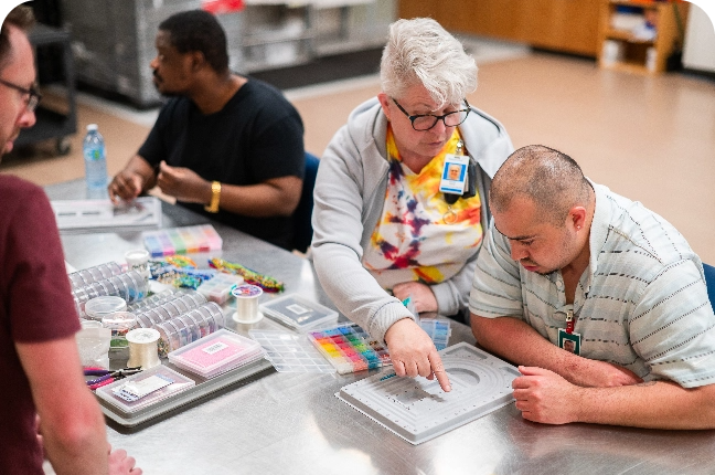 A woman and three men sitting at a table with assorted coloured beads.